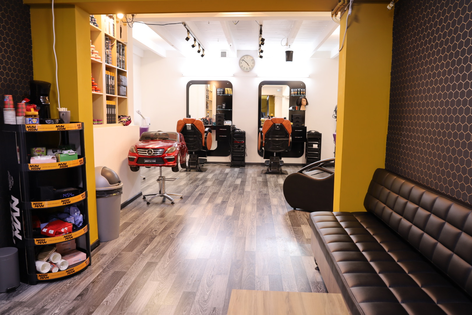 De salon met kappersstoelen, spiegels en een zwarte zitbank